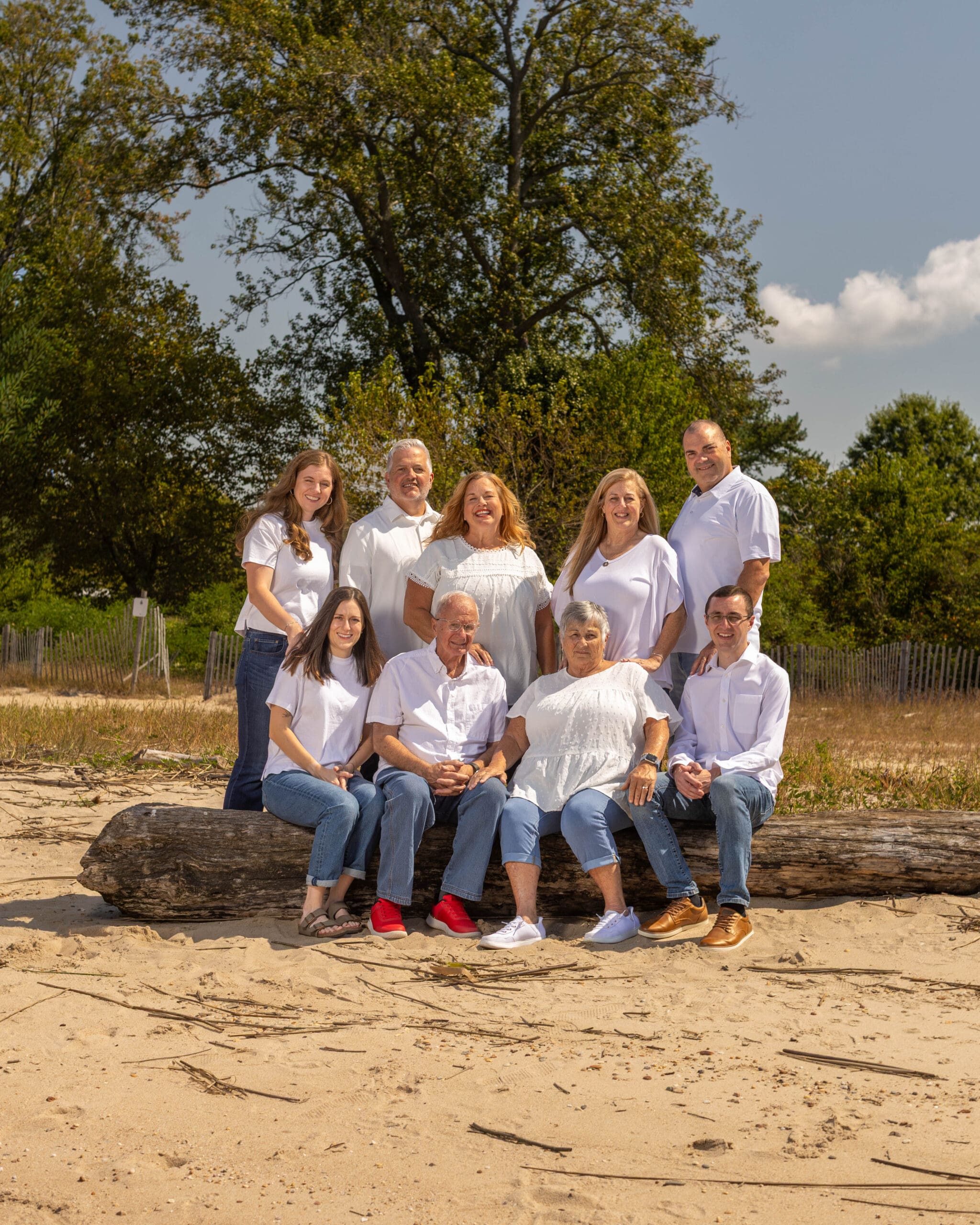 A group of extended family sitting on a big log on the beach for a family portrait.