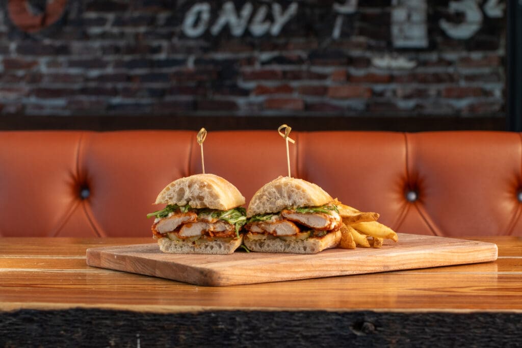 A chicken sandwich sitting on a wooden table in a rustic bar.