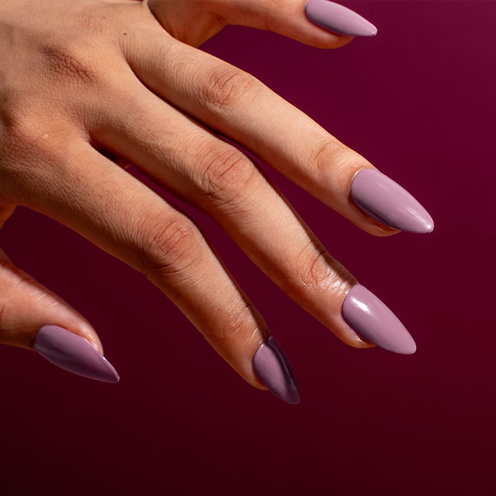 A female hand model with a dusty purple gel polish on a maroon background.