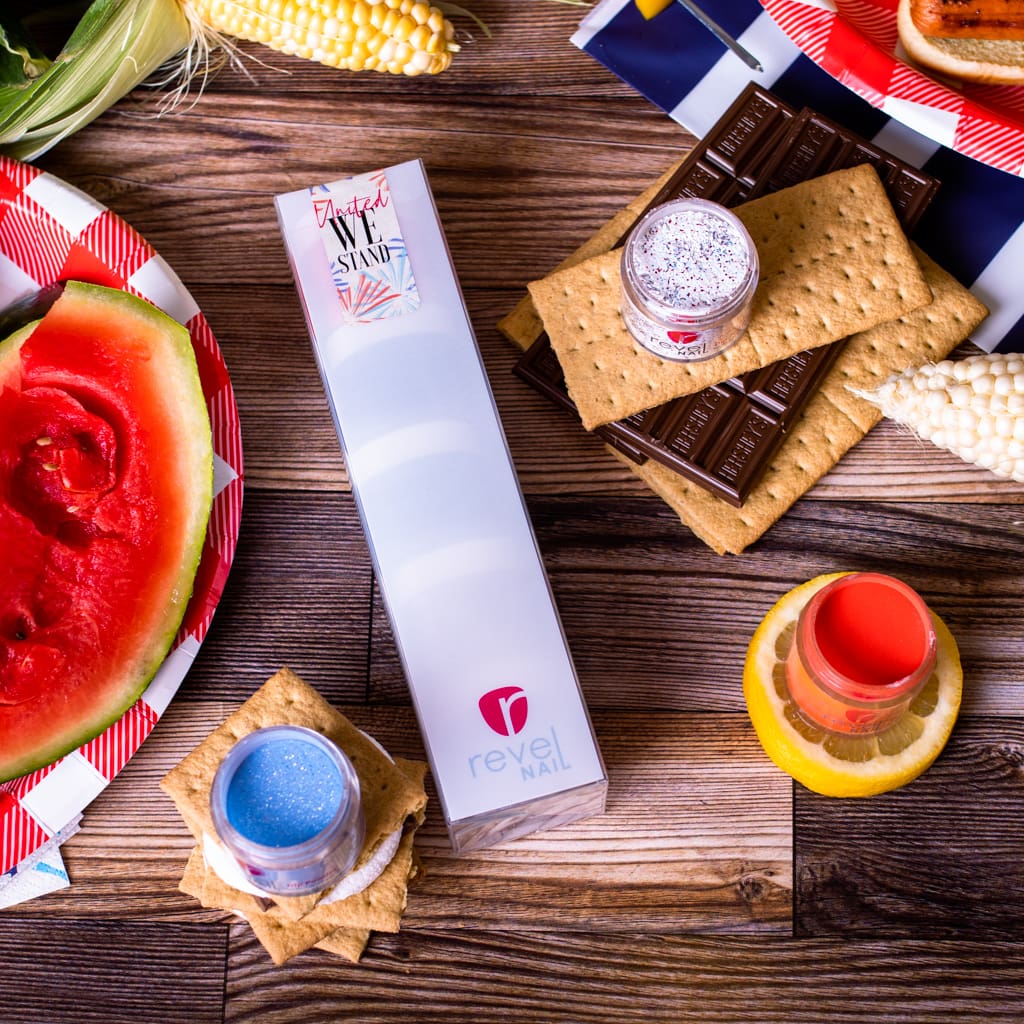 A dip powder nail set laying on a table with summer barbecue foods around it.