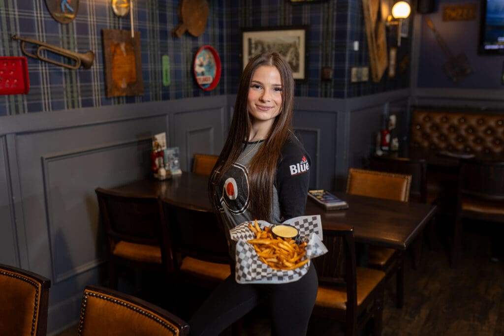 A female server in a Flyers shirt holding fries in a pub.