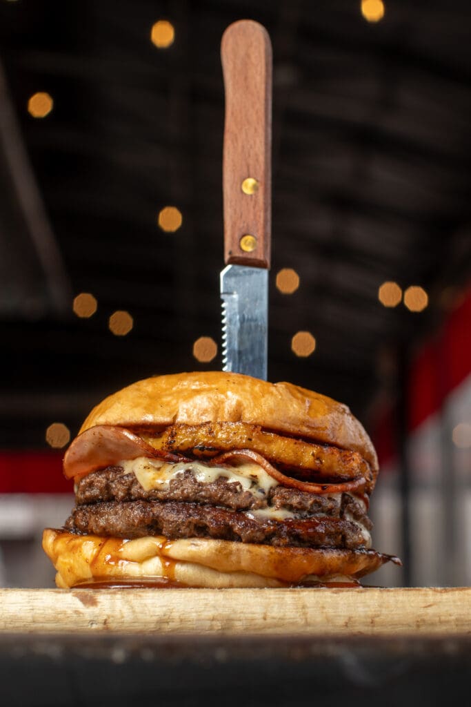 Burger sitting with a steak knife through the top at a hero angle photograph.