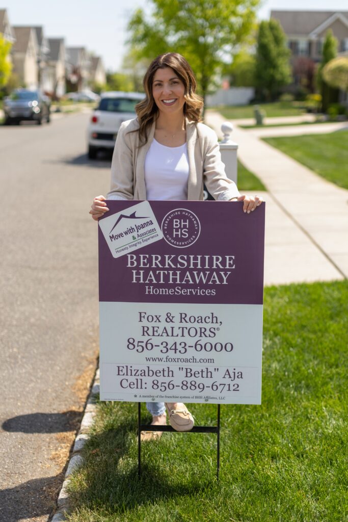 A South Jersey Realtor for Berkshire Hathaway, placing a for sale sign in a lawn while smiling at the camera for a branding photography session.
